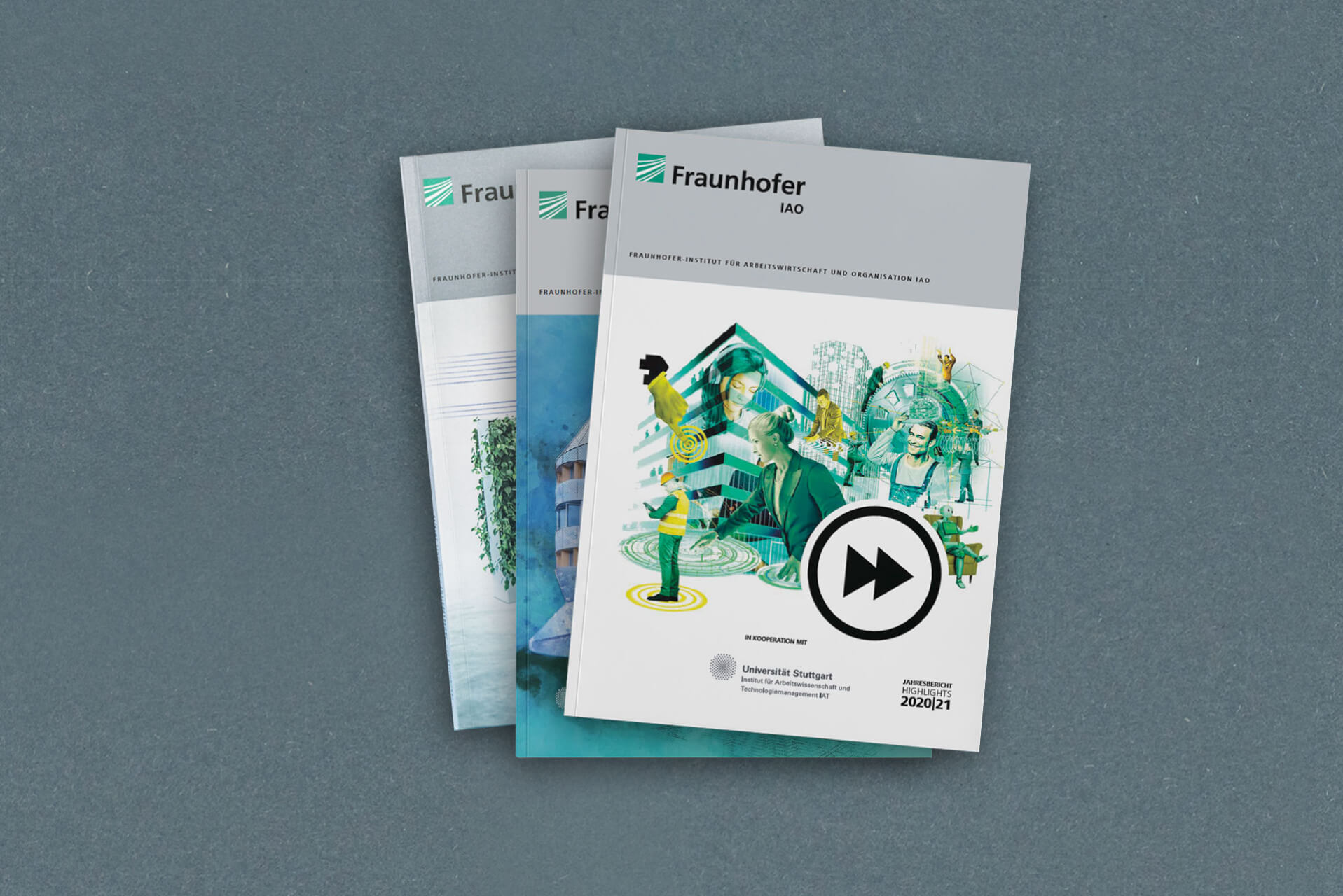 Alle Fraunhofer-Jahresberichte liegen aufgestapelt übereinander, der aktuelle liegt ganz oben. Das Cover ist eine Collage aus einem großen Bürogebäude sowie Menschen und ihrer Arbeit, die von technischem Fortschritt geprägt ist.